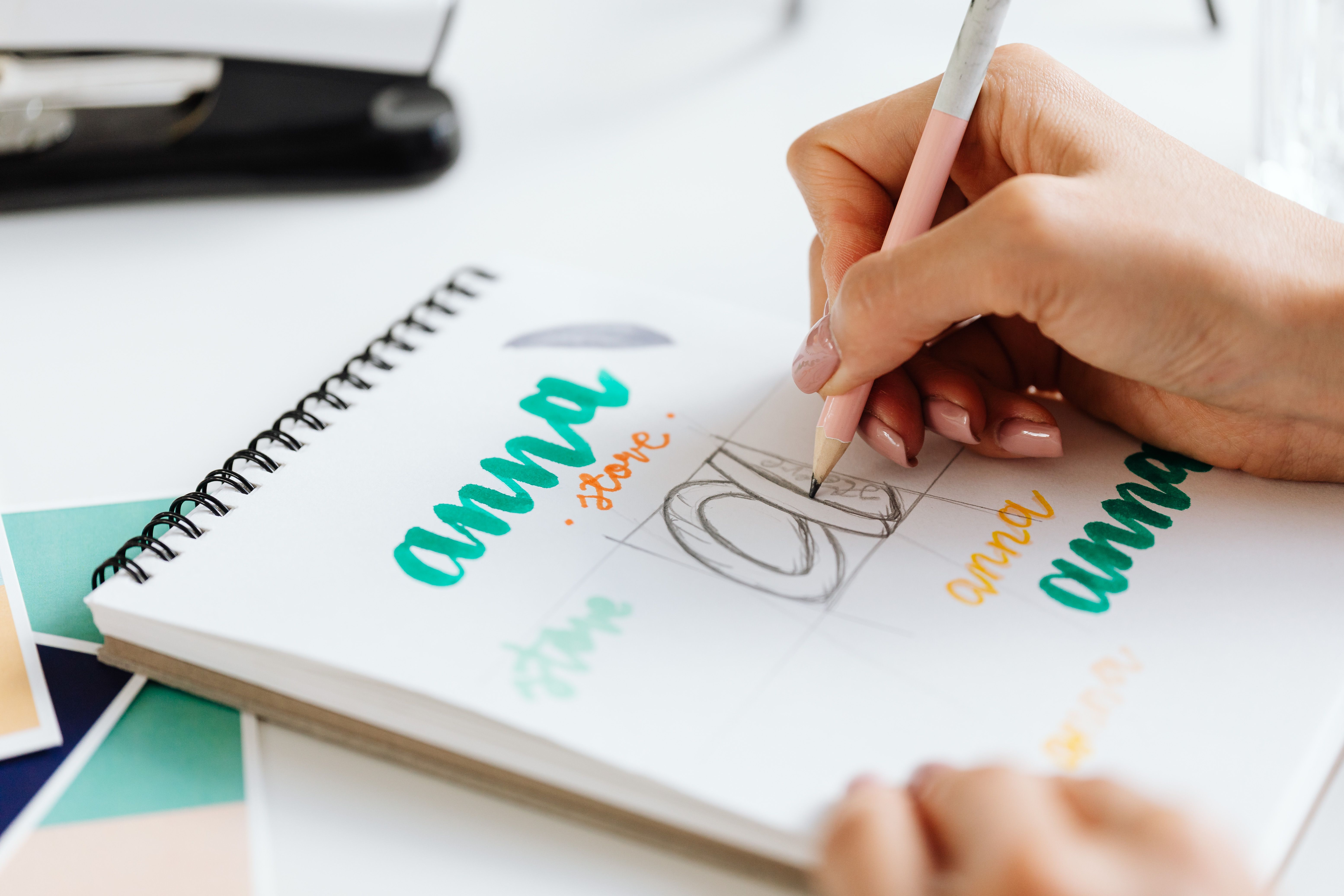 A designer sketching a logo in a notebook beside colour swatches